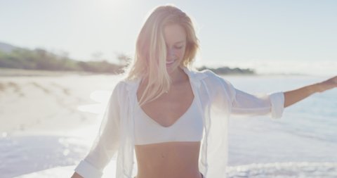Young attractive woman smiling and walking on the beach at sunrise on her tropical vacation, happy blonde woman enjoying the beach