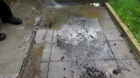 A male adult uses a pressure washer lance to clean a garden path that has collected slime and grime over many years.
