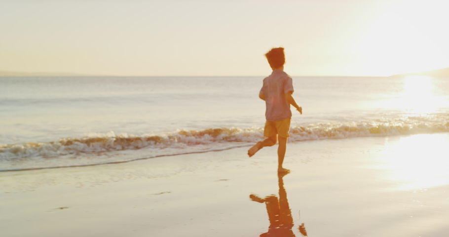 Young toddler boy running and jumping and splashing joyfully on the beach at sunset