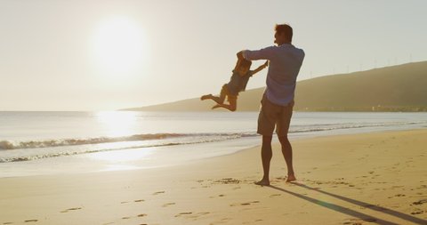 Dad swinging his toddler son into the air on the beach having fun at sunset, multi ethnic father playing with his young son at the beach, priceless parenthood moments, father son silhouette