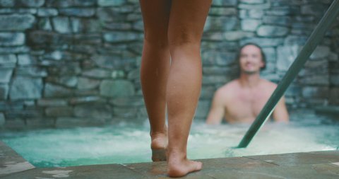 Attractive multi ethnic woman walking into a hot tub with her young attractive boyfriend smiling at her, happy couple enjoying a hot tub together