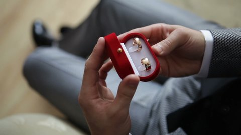 Elegant young groom puts gold wedding rings in a red box.
