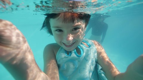 Child girl is playing underwater, looking at camera and making bubbles.