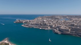 Flies backwards over Fort Manuel, the capital of Malta, Valletta and the Mediterranean Sea in front, historic buildings and boats in the background. Aerial video