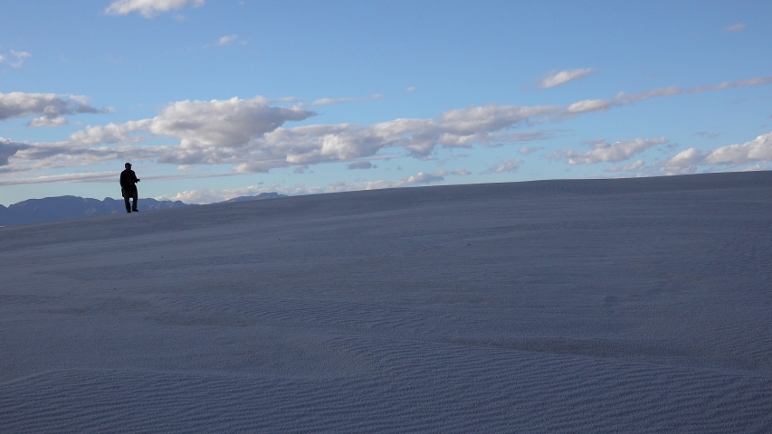 People walk on white gypsum sands in a desert landscape against a background of white clouds. Sand Dune at White Sands National Monument. New Mexico, USA