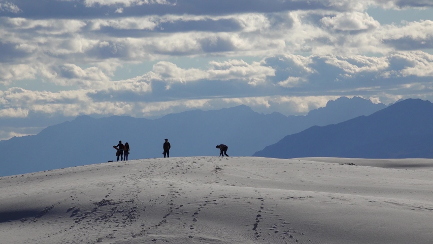 People walk on white gypsum sands in a desert landscape against a background of white clouds.  Sand Dune at White Sands National Monument. New Mexico, USA