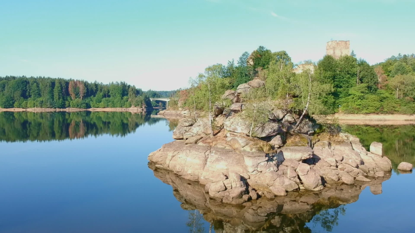 Rock in a Lake in front of Forest under blue Sky sourrounded with blue Water. Drone shot of Recreational Lake.