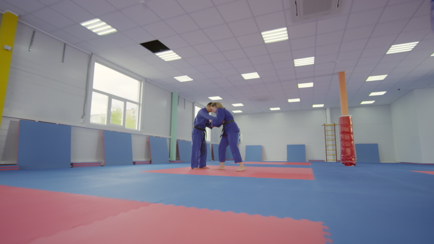 Zoom in slow motion shot of professional female jiu-jitsu athlete in blue ji throwing male partner over shoulder and doing lockdown while training together in martial arts gym Royalty-Free Stock Footage #1043783194