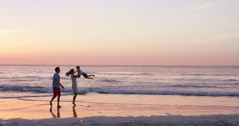 Happy family on the beach holding hands swinging little girl around at sunset on vacation slow motion RED DRAGON