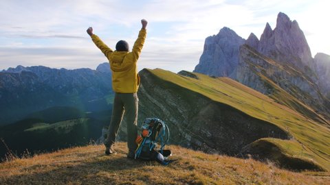Young man hiking at Seceda mountain raising arms to the sky on the peak at sunrise. Traveling to puez Odle, Dolomites, Trentino, Italy.