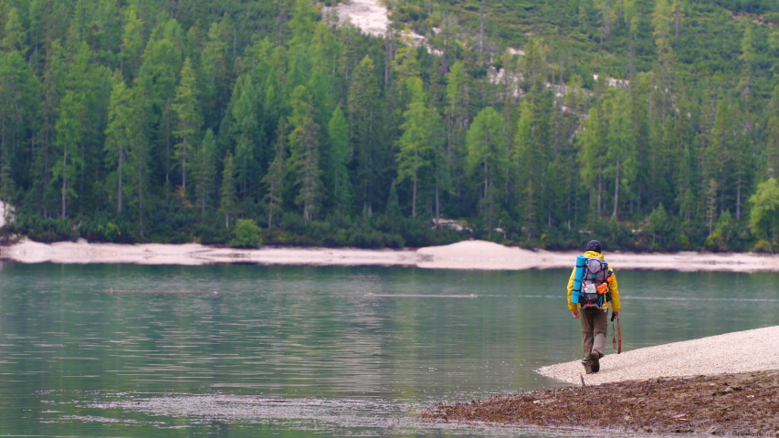 Young tourist hiker man walking at beautiful alpine lake Lago Di Braies (Pragser wildsee) in Trentino. Traveling Dolomites mountains, Italy.