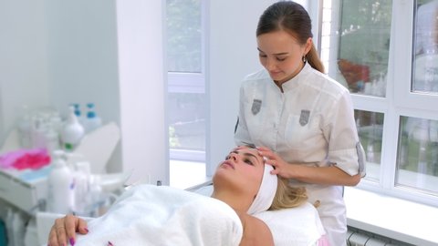 Cosmetologist preparing client woman to cosmetic beauty procedure putting headband. Beauty treatment in spa center. Portrait of woman lying on settee. Beautician adjusts hairs of client.