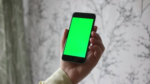 Phone image. Green screen. It is held with the left hand. Iphone 6S. Upright screen. Watching videos. Browse photos and social media. Day and in the room. Checking your mails.