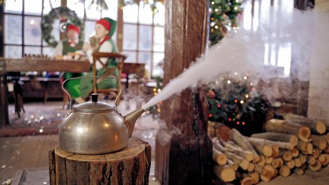 Boiling retro aluminium kettle. Teapot steams. Two elves on the background. New year spirit. Christmas eve. Closeup. Teapot on a log.
