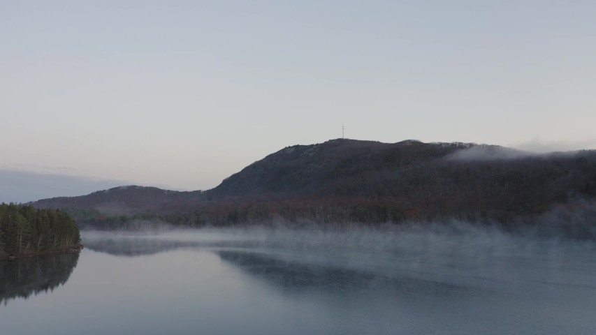 Panning across the suface of a misty lake with a mountain in the distance AERIAL