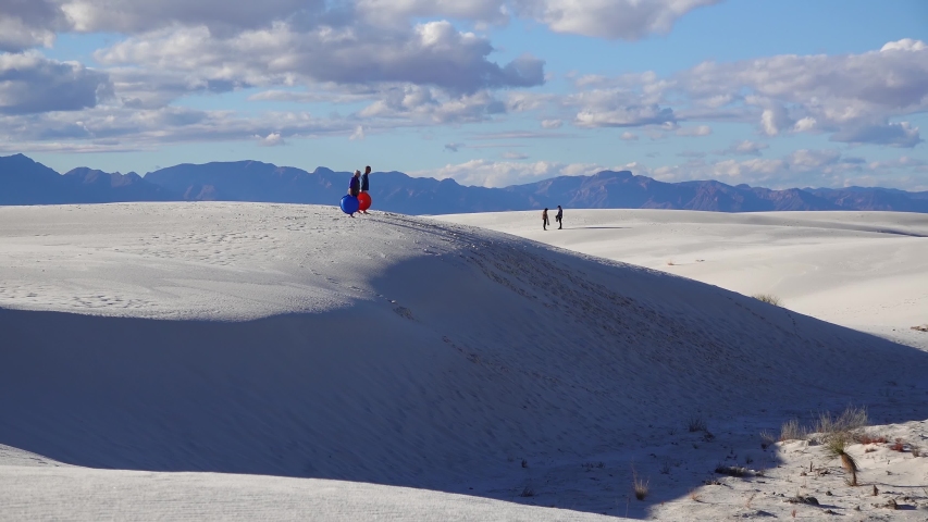 People walk on white gypsum sands in a desert landscape against a background of white clouds.  Sand Dune at White Sands National Monument. New Mexico, USA