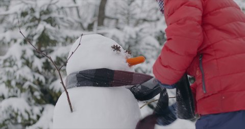 Cute little Caucasian kid putting a scarf on a snowman, boy playing outside in winter. 4K UHD RAW Graded footage Video de stock
