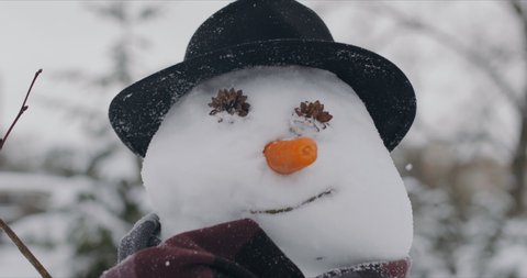 Funny snowman dressed in stylish hat and black scarf standing in the street in winter