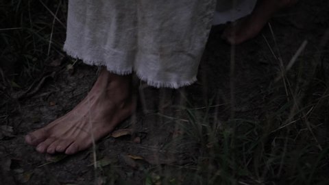 Closeup of robed mans feet or Jesus walking through forest trees. Dramatic and moody. Slow motion.
