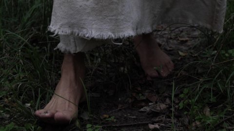 Closeup of robed man or Jesus walking through forest trees. Dramatic and moody. Closeup of feet. This could be used for a fantasy movie... wizard, jedi or something else like that.