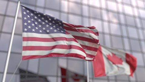 Waving flags of the USA and Canada in front of a modern skyscraper facade