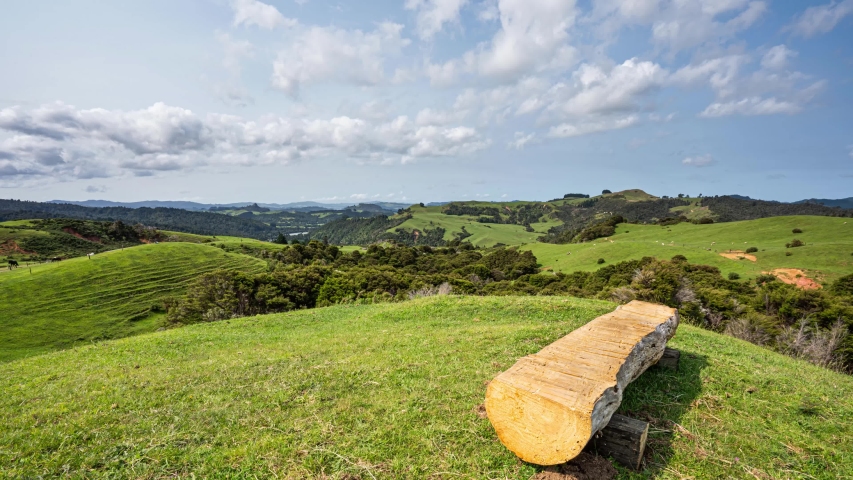 a timelapse of the clouds going by over a static foreground of a banch over a grassy hilly farm land