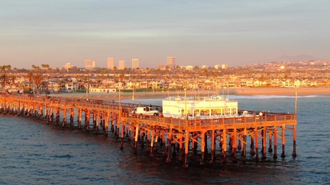 Cinematic aerial view of the pier in Newport Beach, Orange County in California on sunny afternoon during golden hour with peninsula and harbor in view.