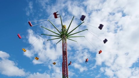 People enjoying the swing ride in amusement park against blue sky with white clouds in slow motion