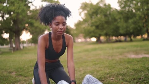 Portrait of An african american young woman assisting her friend doing sit-ups at park - friend motivating her friend to keep going and push herself to the next level