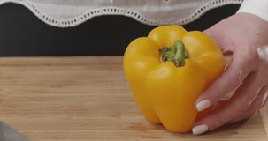 Closeup of woman hands removes top and core of yellow bell pepper on wooden board in a modern kitchen. . The girl puts the vegetables in a salad bowl. Prepare a salad. Shot on 6k Blackmagic camera.