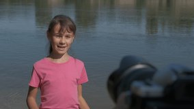 Shoot video by the river. Nice child describe something on camera by the water.