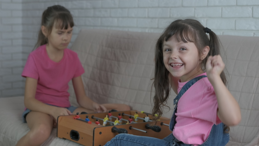 Enjoy table football. Smiling little girl beat her sister in table football game in the room.