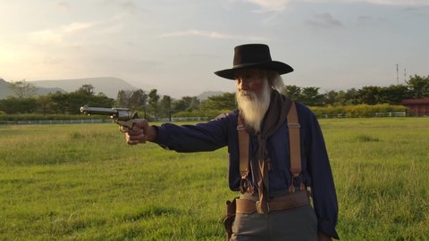 One old cowboy playing and spinning revolver in the yard and points the weapon left and right.