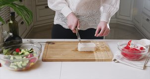 Closeup of woman hands cutting feta cheese on wooden board in a modern kitchen. Healthy diet. Macro. Prepare a salad. Shot on 6k Blackmagic camera.