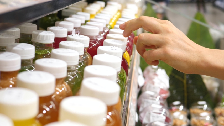 Woman Hand Selects Fresh Squeezed Juice In Plastic Bottle At Supermarket. Closeup.