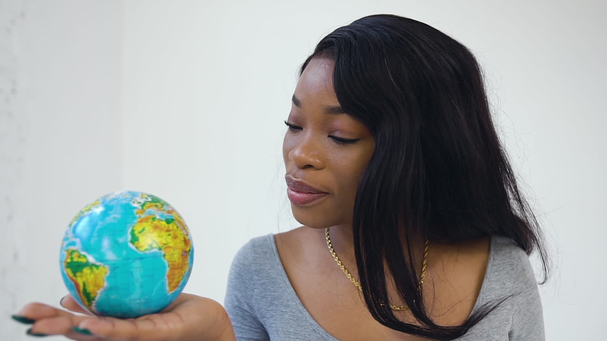 Close view of charming joyful african american young girl with long wavy hair which posing on camera with little globe on hand