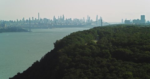 Aerial view of lush green forest on island with Manhattan skyline in the background in New York during the day under overcast blue sky. Wide shot on 4K RED camera.