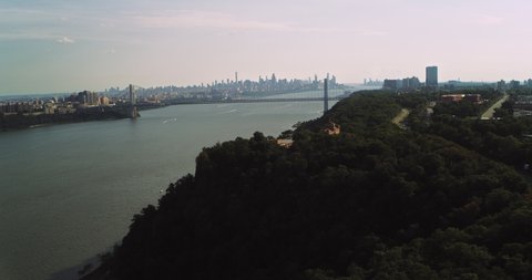Aerial view of lush green forest on island with Manhattan skyline in the background in New York during the day under overcast blue sky. Wide shot on 4K RED camera.