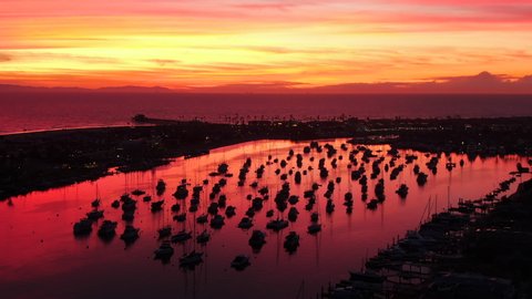 Cinematic aerial view of the harbor, ocean and pier in Newport Beach, Orange County in California with boats below during a red and pink sky twilight