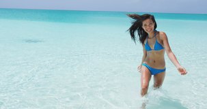 Travel Vacation Woman Happy Enjoying Summer Beach Holidays Jumping Having Fun Running Out Of Water Splashing Laughing Smiling. Beautiful woman in white bikini.