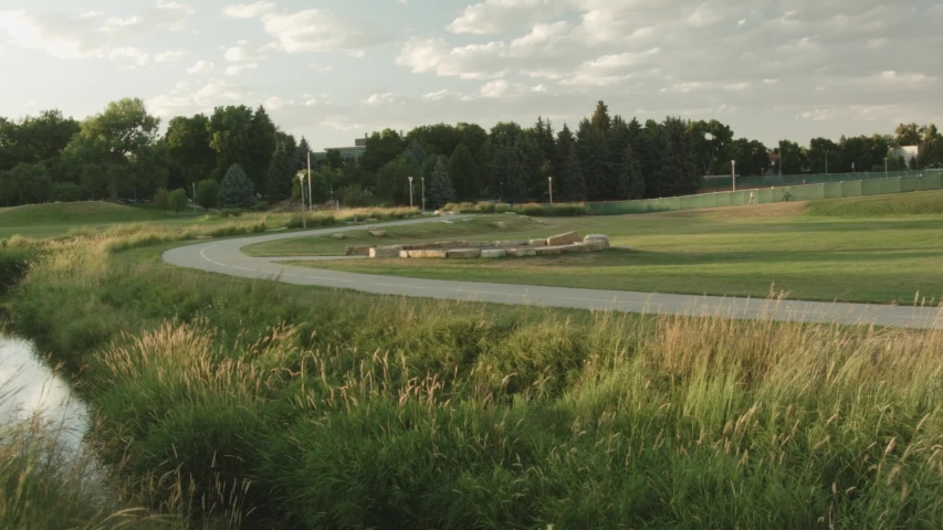 Open park with a stream, tall grasses and a paved bike path curving across the landscape