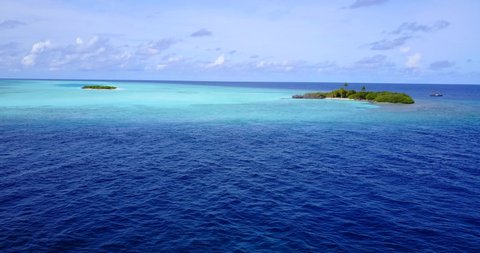Turquoise lagoon across tiny tropical island surrounded by deep blue ocean under dusty sky in Maldives