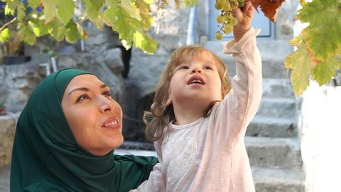 Happy muslim mother in hijab playing with her daughter in the garden. Arabic happy family lifestyle moments