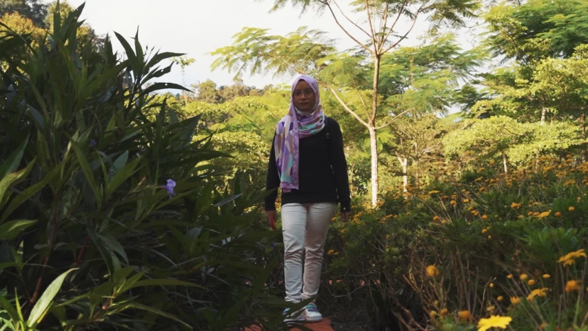 Attractive young Muslim woman enjoying view of green park with beautiful flowers at Cameron Highlands, Pahang