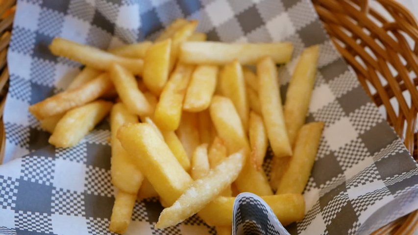 French fries served in a small basket placed on wooden table.