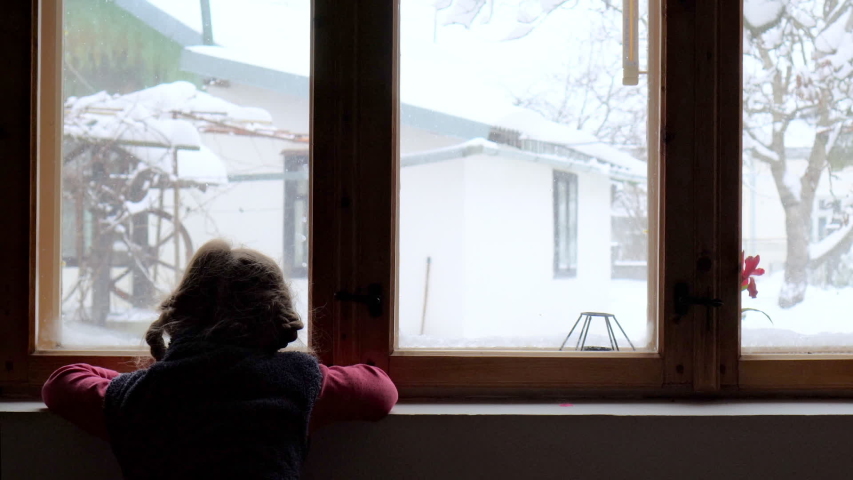Silhouette of a child lookin for somebody at the window. Girl waiting Santa Claus. Child watching snow falling.  