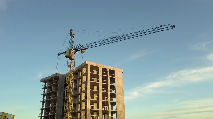Aerial view of concrete frame of tall unfinished apartment building under construction in a city.