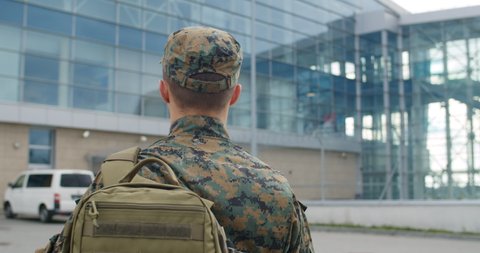 Back view of male soldier leaving on military service. Man in military uniform putting bag on shoulder and walking to airport terminal. Concept of military service, army, duty
