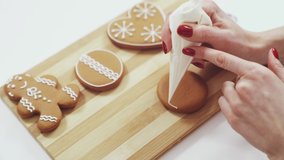 Young woman with red trendy manicure accurately decorating brown ginger cookies in various shape with sugar glaze. Concept of homemade baking and tasty christmas pastry