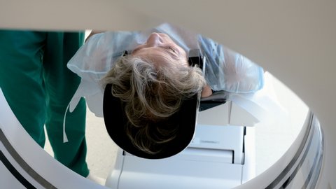 Close-up shot of a female mature patient lying on a table of CT scan machine. Computer tomograph scanning body and brain of elderly woman. High-tech equipment in medical clinic. 4K